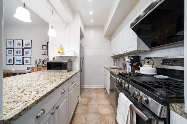 kitchen with white cabinets, light stone counters, range hood, stainless steel appliances, and a sink