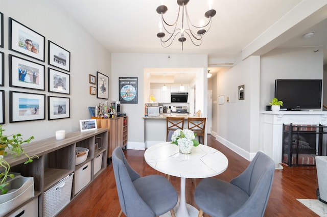 dining area with dark wood-type flooring, a brick fireplace, baseboards, and an inviting chandelier