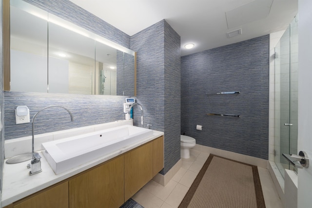 bathroom with vanity, a shower with door, tile patterned floors, toilet, and tile walls