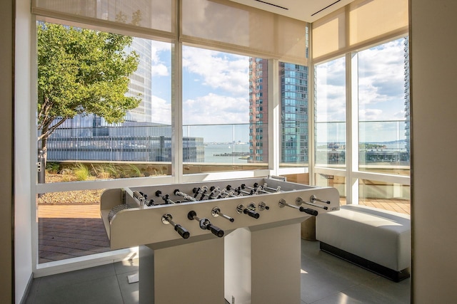 game room with tile patterned flooring, a water view, and a wall of windows