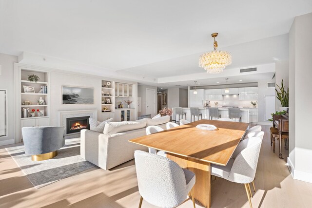 dining space featuring visible vents, a tray ceiling, light wood-style floors, a fireplace, and a notable chandelier