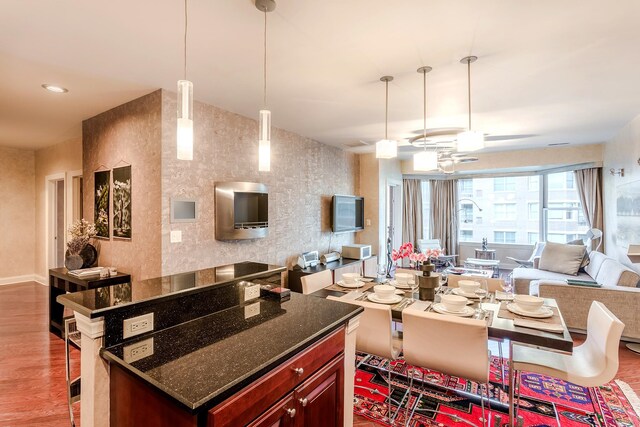 kitchen featuring wood-type flooring, dark stone counters, decorative light fixtures, and a breakfast bar