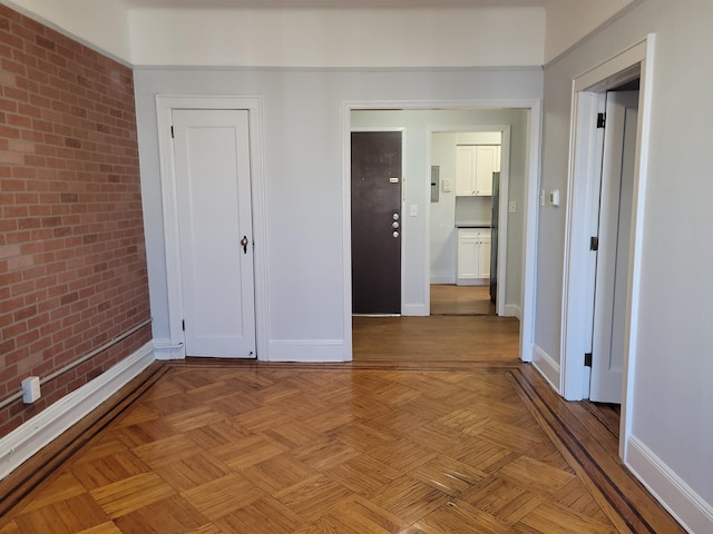 unfurnished bedroom featuring light parquet flooring and brick wall