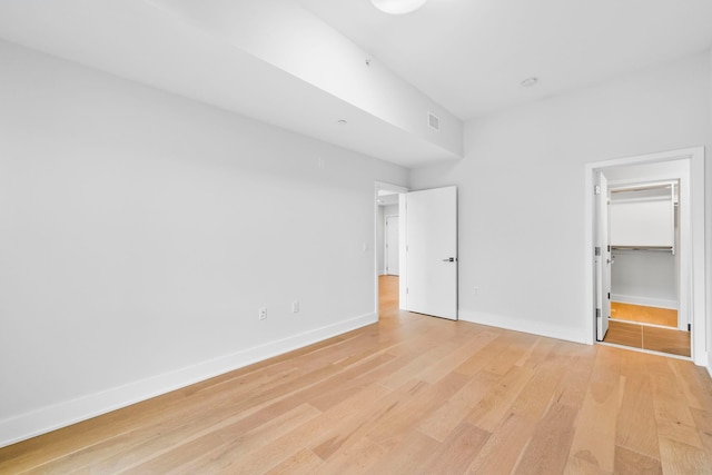 unfurnished bedroom with light wood-style floors, visible vents, a spacious closet, and baseboards