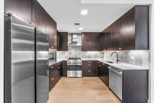 kitchen with stainless steel appliances, a sink, wall chimney range hood, and tasteful backsplash