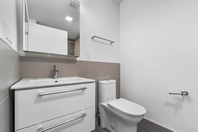 bathroom featuring toilet, visible vents, tile walls, and vanity