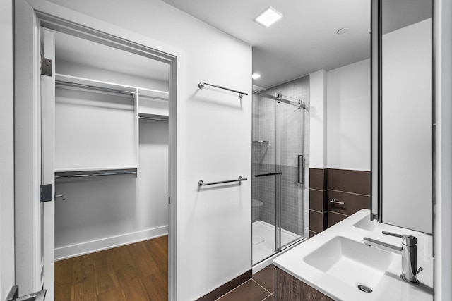 bathroom with a shower stall, a spacious closet, a sink, and wood finished floors