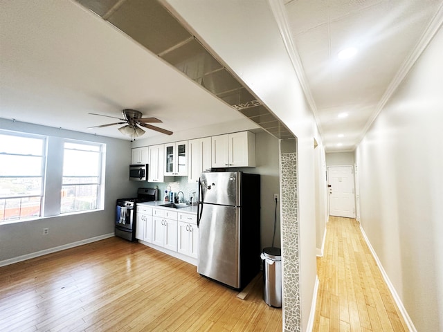 kitchen featuring crown molding, light wood-style flooring, white cabinets, baseboards, and appliances with stainless steel finishes