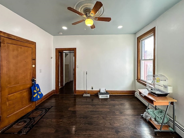 empty room with dark hardwood / wood-style flooring, ceiling fan, and a baseboard heating unit