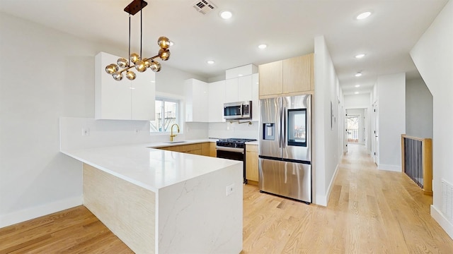 kitchen with light wood finished floors, visible vents, appliances with stainless steel finishes, decorative light fixtures, and light countertops