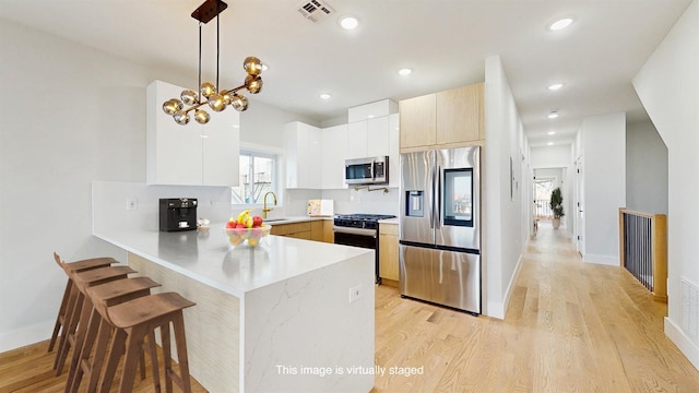 kitchen with pendant lighting, stainless steel appliances, visible vents, light countertops, and a peninsula