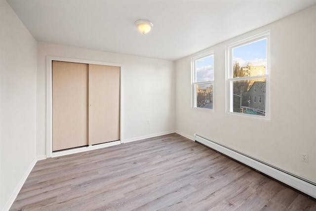 unfurnished bedroom with baseboards, a baseboard radiator, a closet, and light wood-type flooring