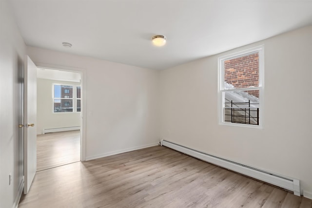 spare room with baseboards, baseboard heating, and light wood-style flooring