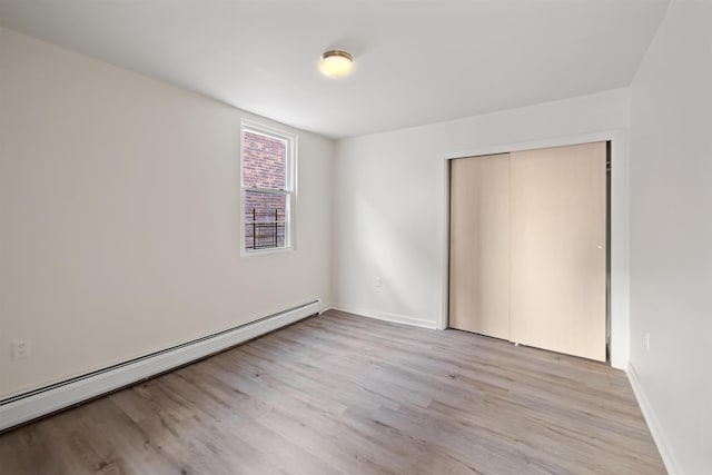 unfurnished bedroom featuring a closet, a baseboard radiator, light wood finished floors, and baseboards