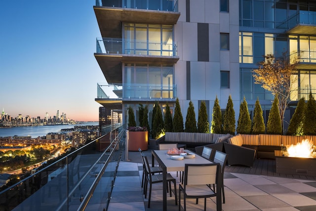 patio terrace at dusk featuring outdoor dining area, a water view, a fire pit, and a city view