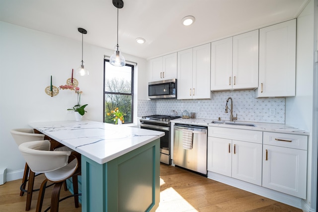 kitchen with tasteful backsplash, white cabinets, a sink, appliances with stainless steel finishes, and light wood-type flooring