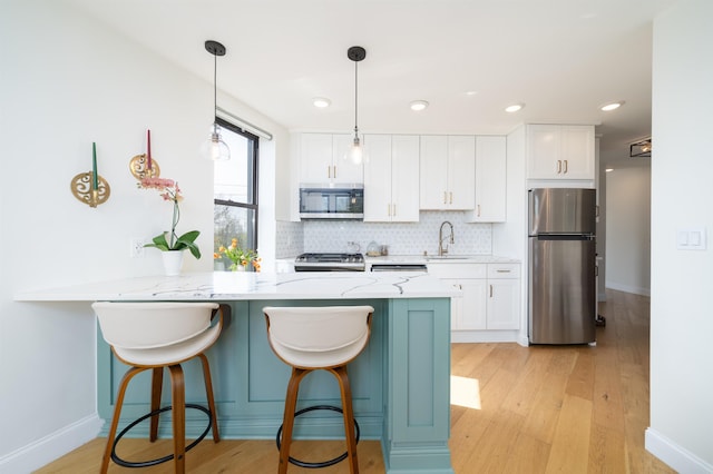 kitchen featuring a sink, backsplash, a peninsula, white cabinets, and appliances with stainless steel finishes