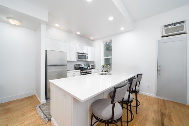 213 8th St, Jersey City, NJ 07302 - kitchen featuring stainless steel appliances, a kitchen breakfast bar, light wood-style flooring, an AC wall unit, and white cabinets