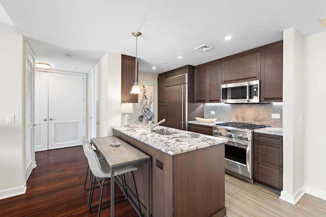 kitchen with pendant lighting, a breakfast bar area, light stone counters, premium appliances, and kitchen peninsula