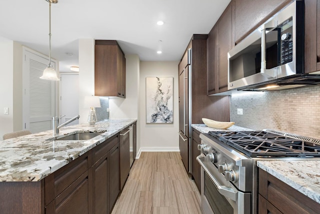 kitchen featuring stainless steel appliances, light stone countertops, sink, and pendant lighting