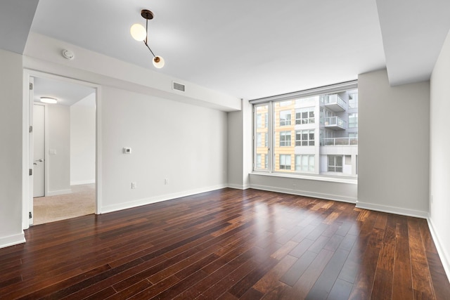 spare room featuring wood finished floors, visible vents, and baseboards