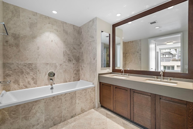 full bath with double vanity, tiled tub, visible vents, and a sink