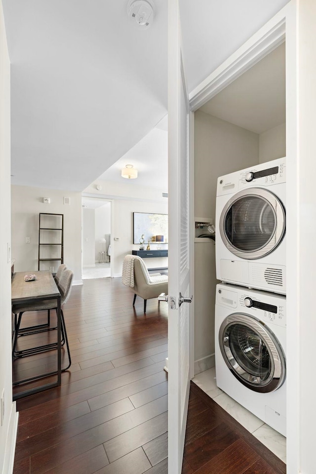 laundry room featuring stacked washer / drying machine, baseboards, and hardwood / wood-style floors