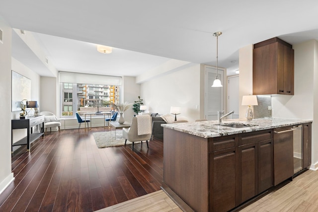 kitchen with open floor plan, light stone counters, wood finished floors, hanging light fixtures, and a sink