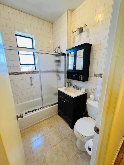 9017 Bergenwood Ave Unit 10, North Bergen, NJ 07047 - bathroom featuring toilet, enclosed tub / shower combo, vanity, tile walls, and tasteful backsplash