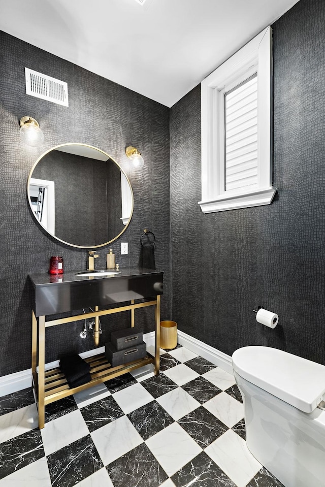 half bath featuring toilet, baseboards, visible vents, and a sink