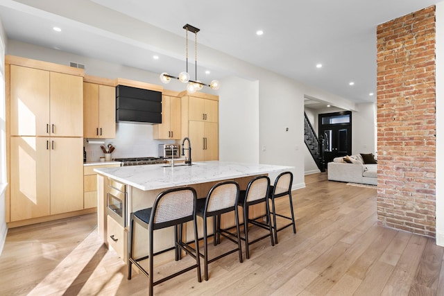 kitchen featuring visible vents, a breakfast bar, light brown cabinetry, a sink, and light wood-style floors