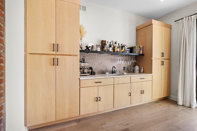 bar with visible vents, light wood-style flooring, a sink, indoor wet bar, and tasteful backsplash