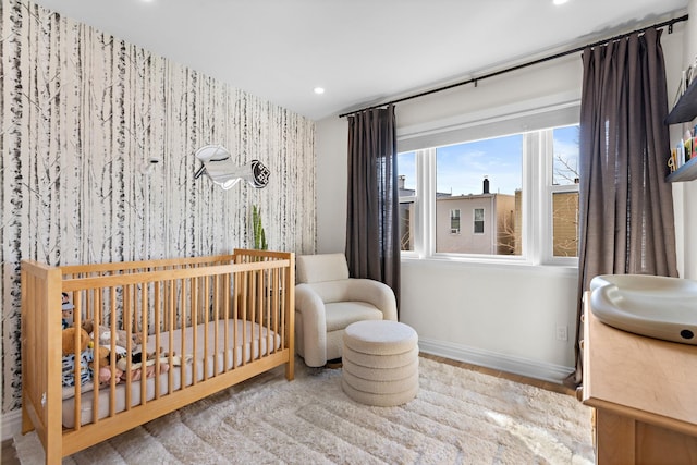 bedroom with baseboards, wallpapered walls, recessed lighting, a crib, and an accent wall