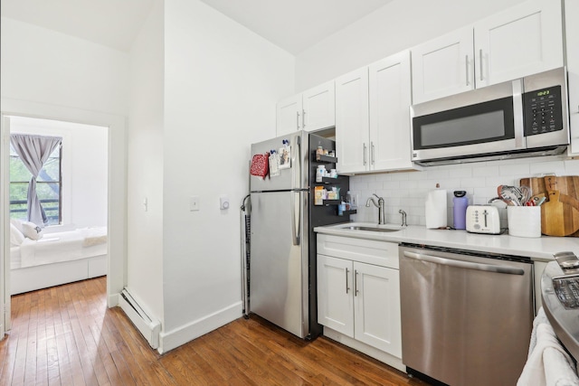 300 Barrow St, Jersey City, NJ 07302 - kitchen featuring a sink, tasteful backsplash, a baseboard heating unit, white cabinets, and appliances with stainless steel finishes