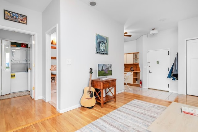 interior space featuring a ceiling fan, stacked washer / dryer, light wood-style floors, and baseboards