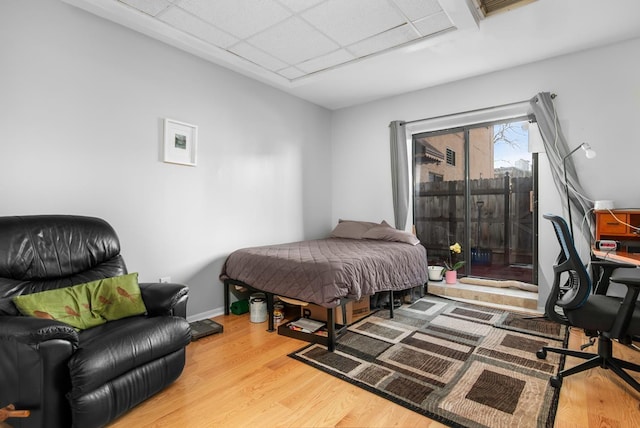 bedroom with baseboards, a paneled ceiling, wood finished floors, and access to outside