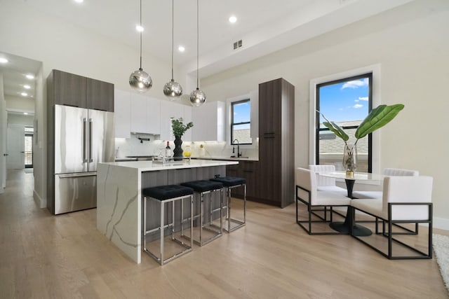 kitchen featuring a center island with sink, hanging light fixtures, decorative backsplash, dark brown cabinets, and high end fridge