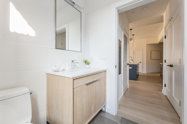bathroom with toilet, tile walls, wood finished floors, and vanity
