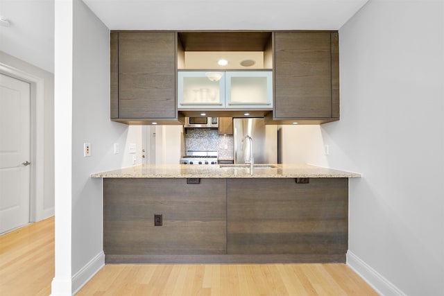 kitchen featuring a sink, light wood-style floors, backsplash, and a peninsula