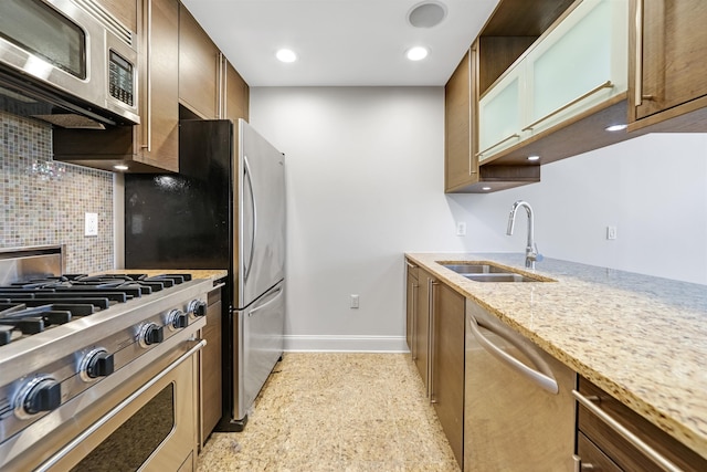 kitchen with backsplash, baseboards, light stone countertops, stainless steel appliances, and a sink