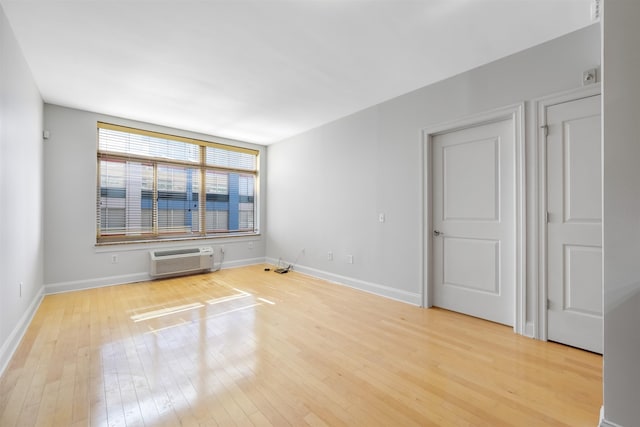 spare room with light wood-style floors, baseboards, and a wall mounted air conditioner