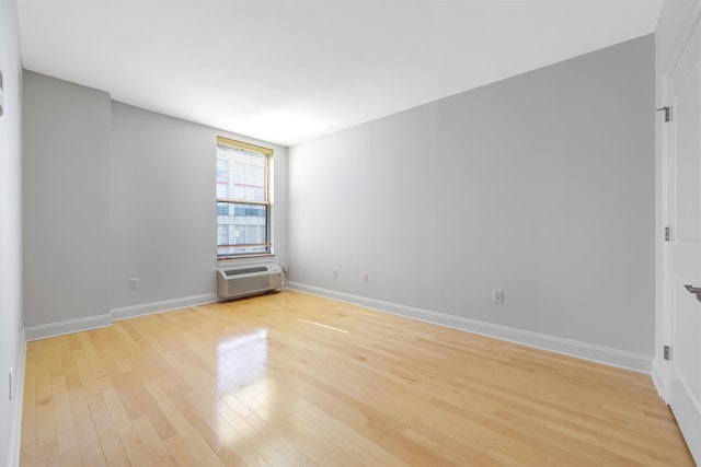 spare room featuring baseboards, an AC wall unit, and light wood-style floors