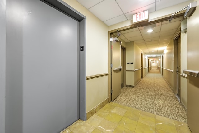 corridor featuring light colored carpet, elevator, a paneled ceiling, and baseboards