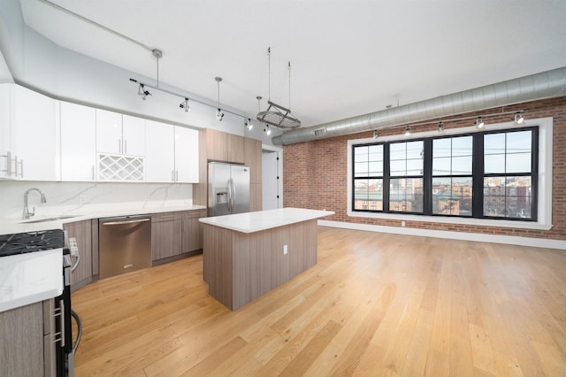 kitchen with sink, light hardwood / wood-style floors, stainless steel appliances, wall chimney exhaust hood, and hanging light fixtures