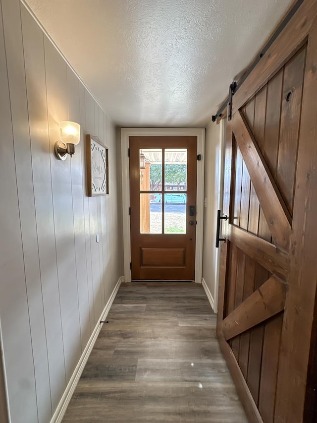 entryway featuring a textured ceiling, a barn door, wood finished floors, and baseboards