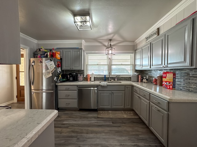 kitchen featuring dark wood-style flooring, stainless steel appliances, gray cabinetry, ornamental molding, and a sink