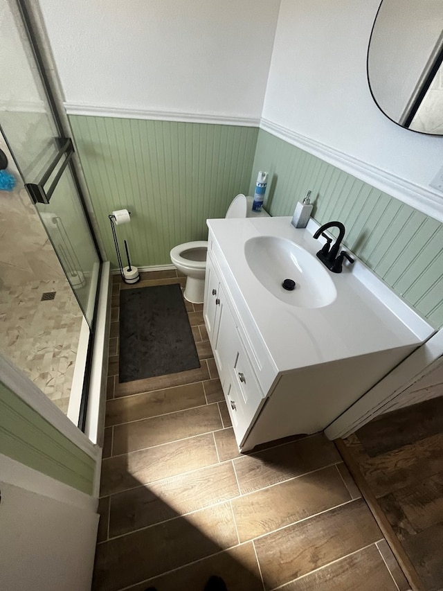 bathroom with toilet, wood walls, a shower with shower door, and vanity