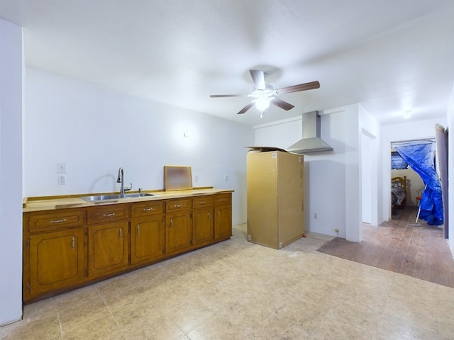 kitchen with ceiling fan, sink, wall chimney exhaust hood, and light hardwood / wood-style flooring