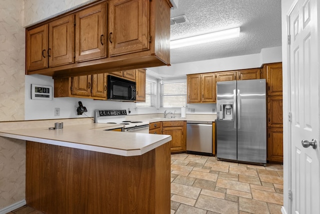 kitchen with a kitchen bar, sink, a textured ceiling, appliances with stainless steel finishes, and kitchen peninsula