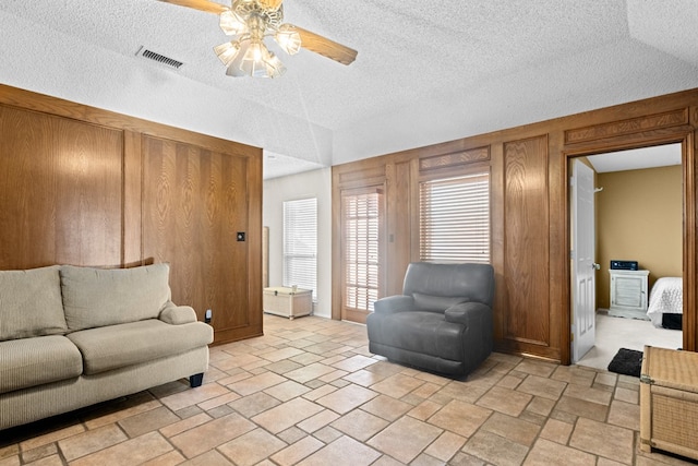 living room featuring ceiling fan, a textured ceiling, and wooden walls